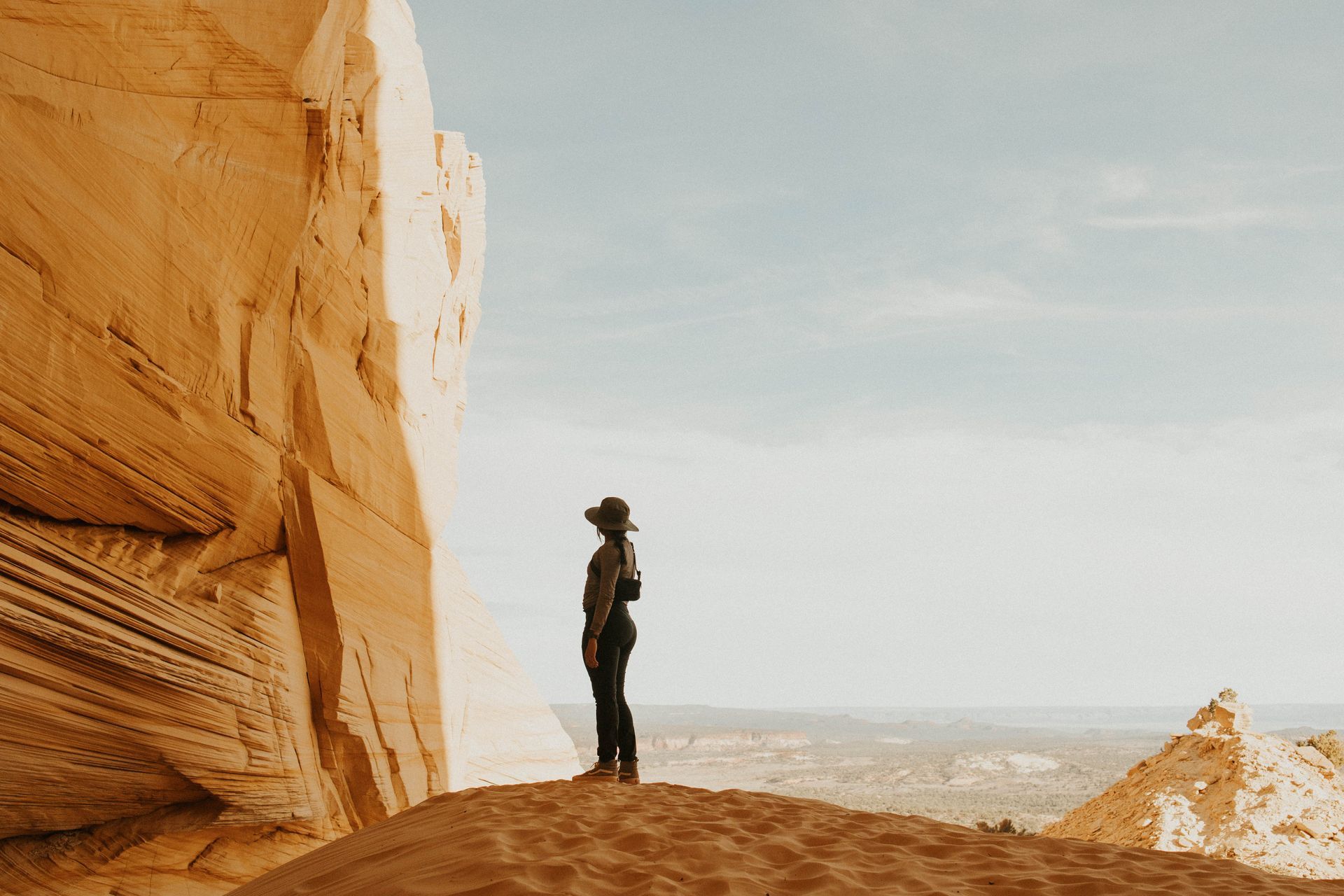 A man in a hat is standing on top of a sand dune in the desert.