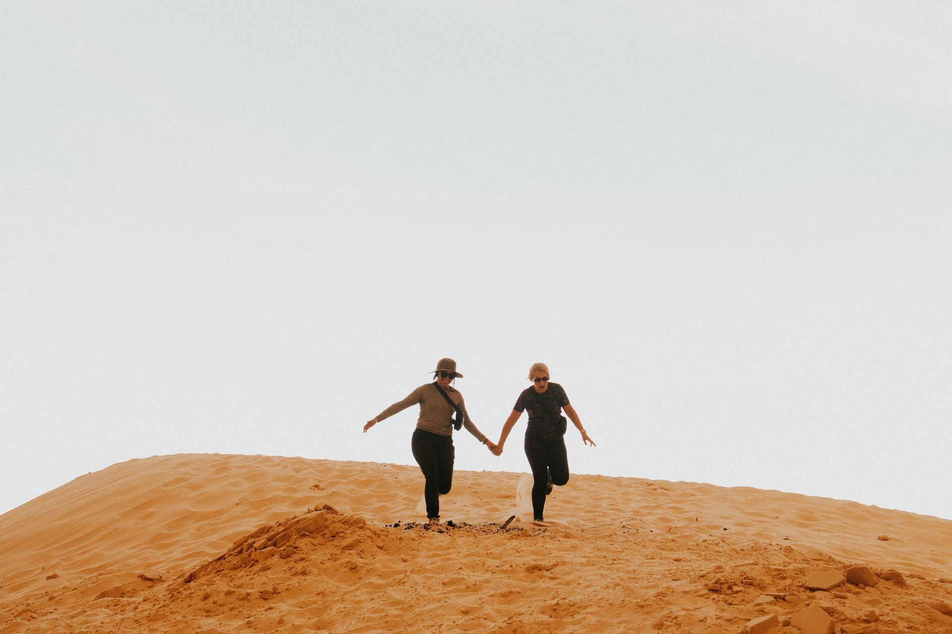 Two people holding hands running in the sand