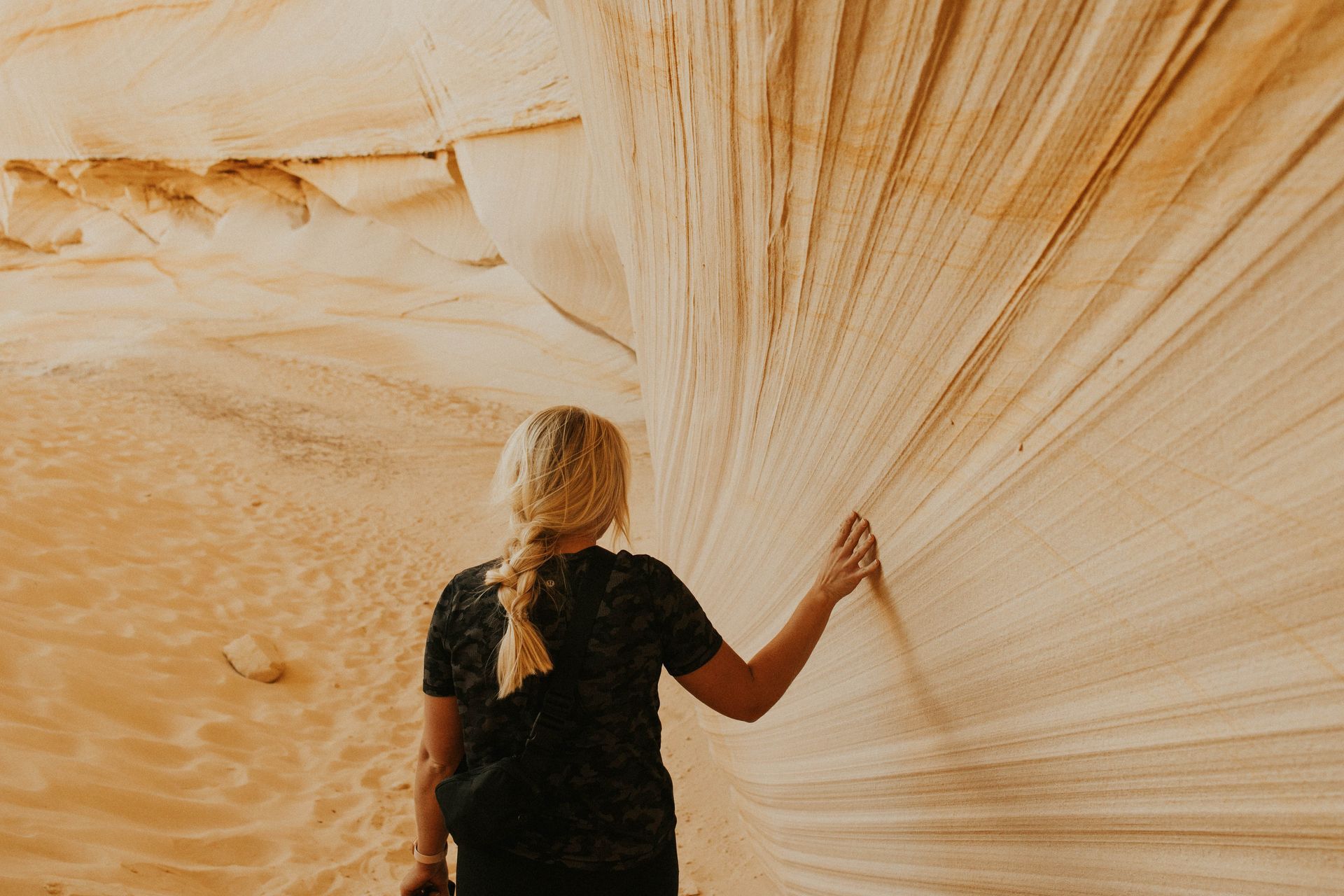 A woman is standing in front of a large rock wall in the desert.