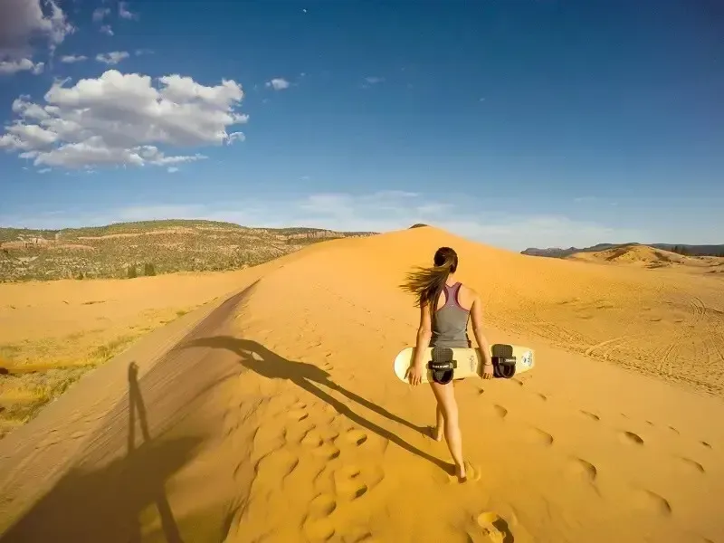 Person walking on a sand dune in a desert under a blue sky with clouds
