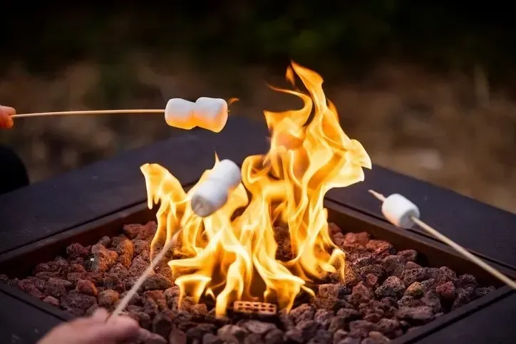 Marshmallows roasting over a crackling fire pit with bright flames and glowing rocks.