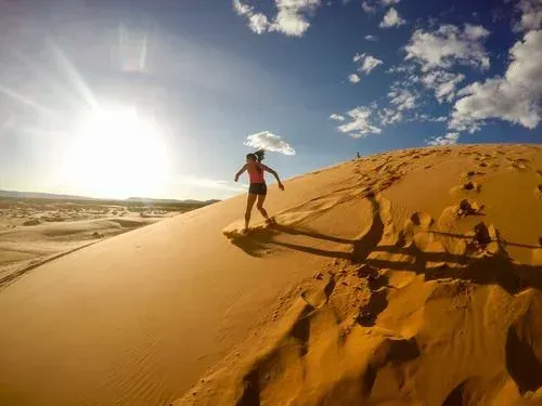 A woman is standing on top of a sand dune in the desert.