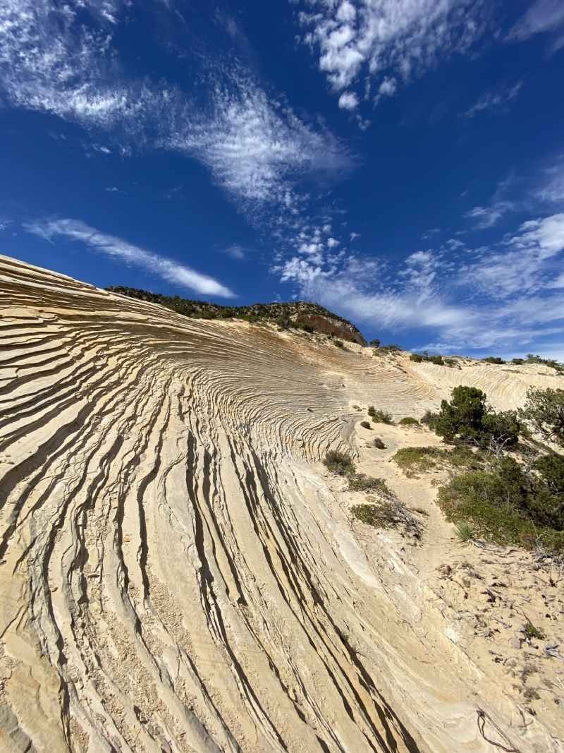 Sandstone cliff with striped patterns under a blue sky with wispy clouds.