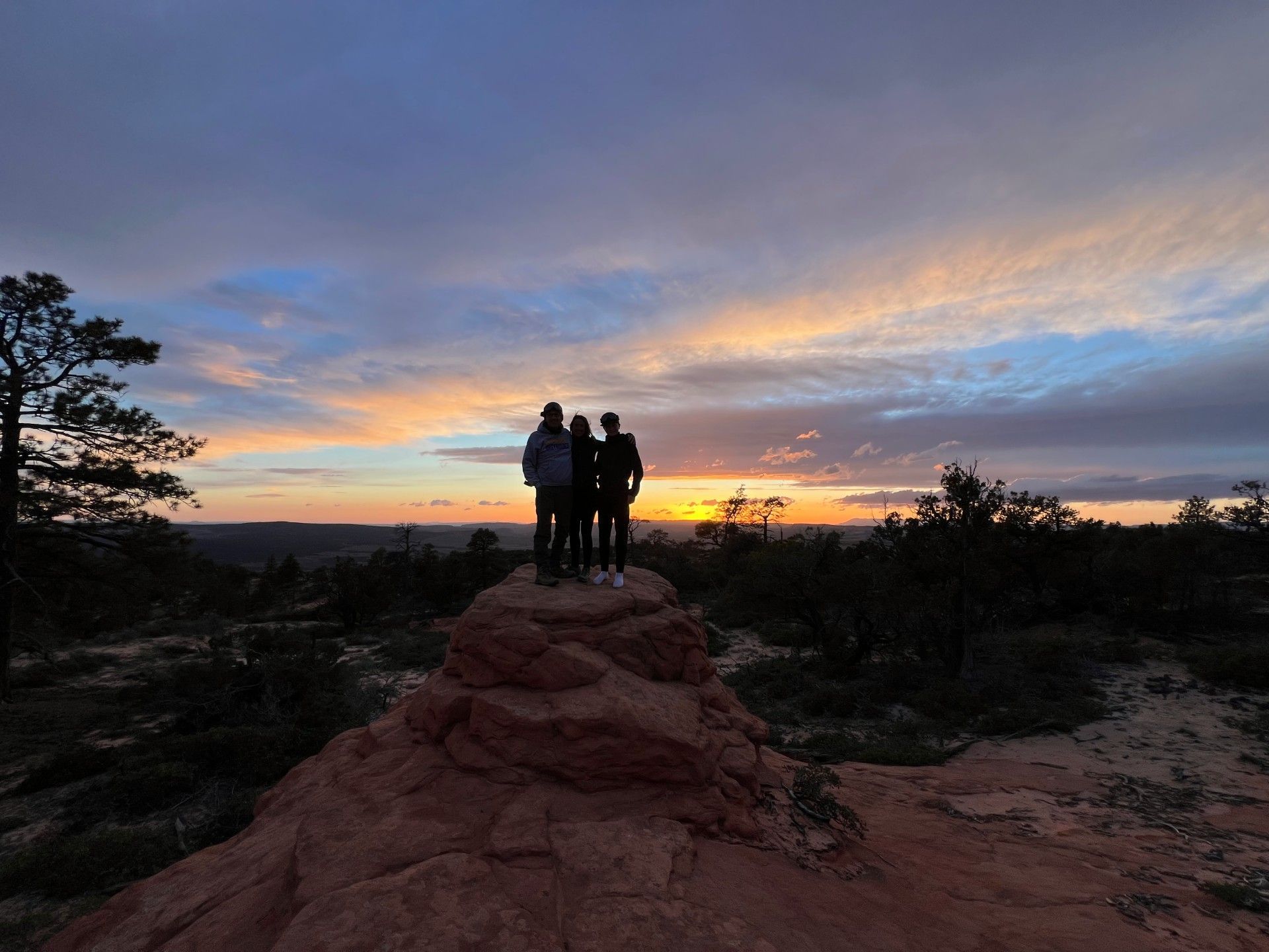 A group of people standing on top of a rocky hill at sunset.