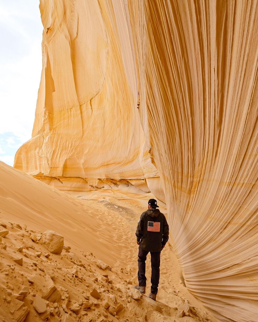 A man is standing in front of a large rock formation in the desert.
