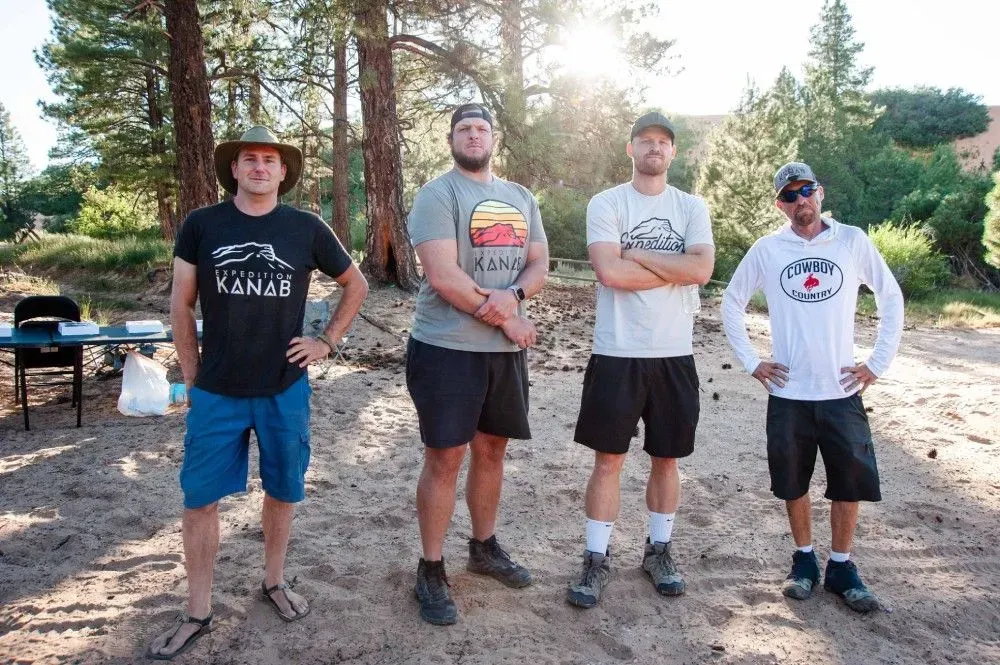 A group of men are standing on a dirt road with their arms crossed.