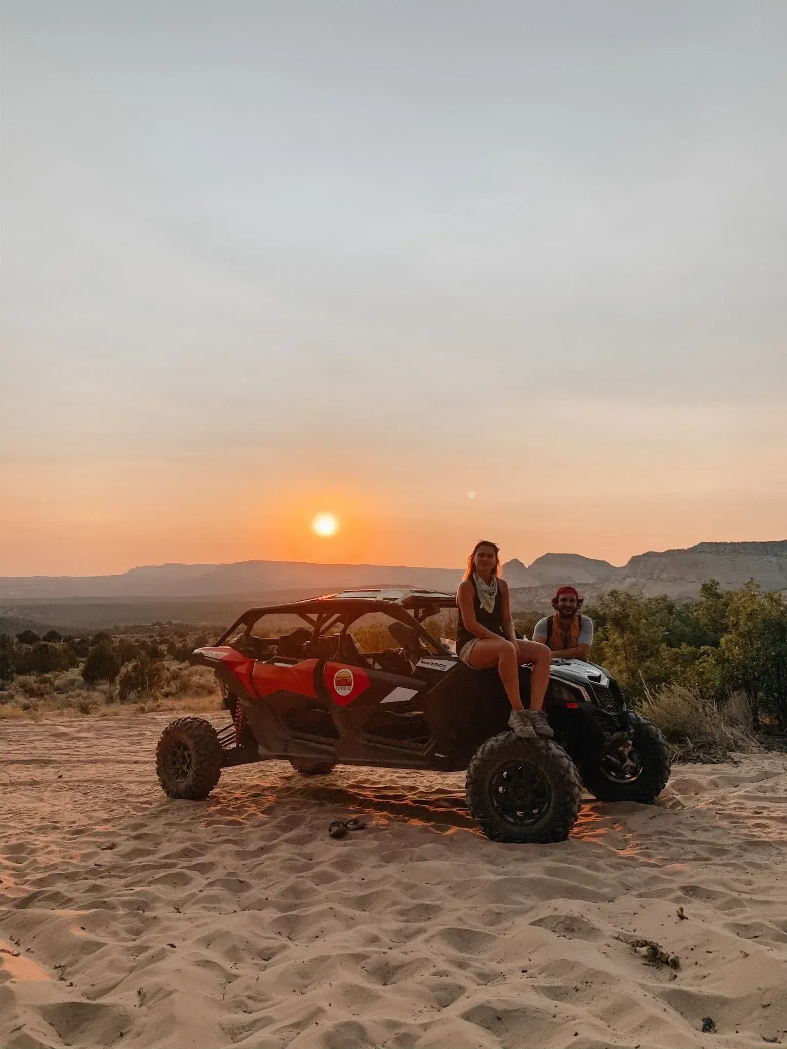 A woman is sitting on the back of a atv in the desert at sunset.