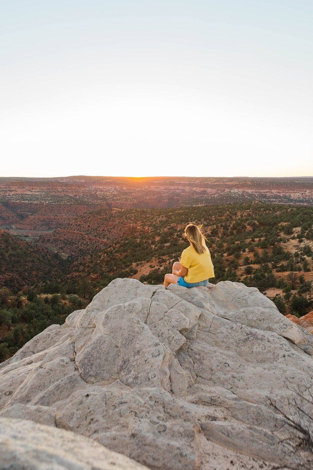 A woman is sitting on top of a rock looking at the sunset.
