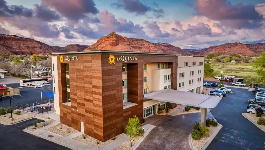 Modern hotel building with wood facade and covered entrance, set against red mountains and a cloudy sky
