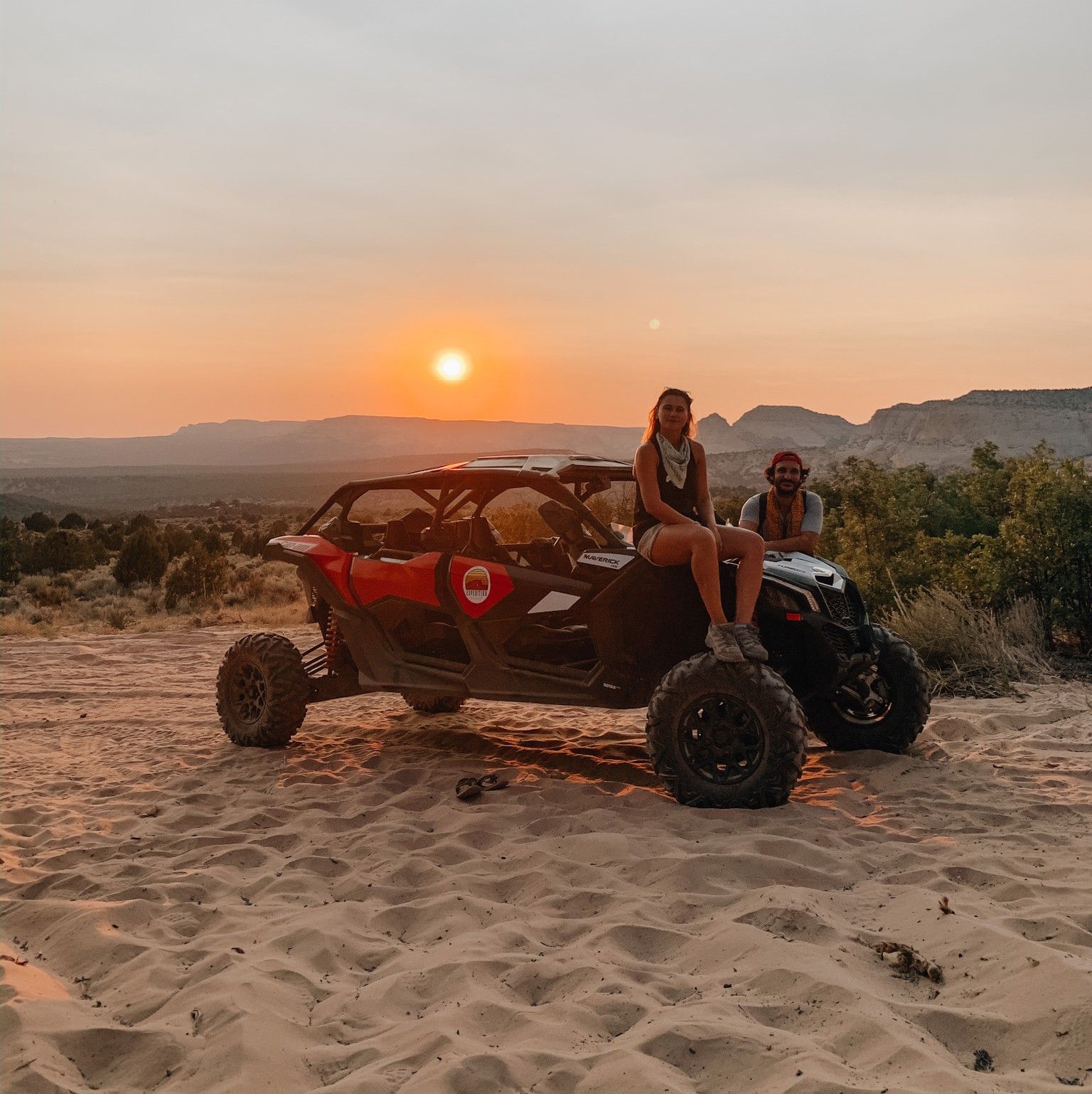 Two women are sitting on top of a atv in the sand at sunset.