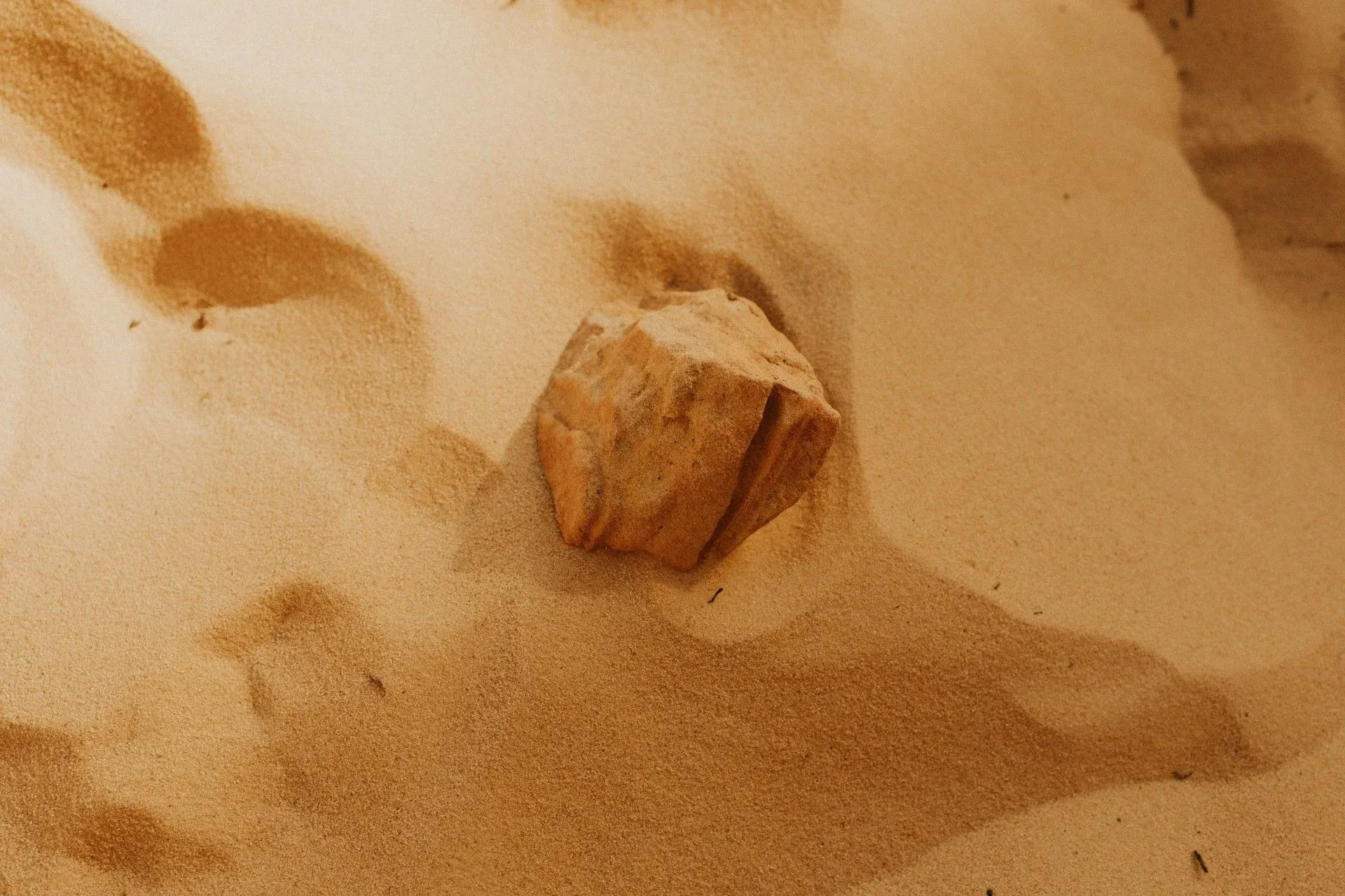 Sand-covered rock partially buried in a rippled desert dune