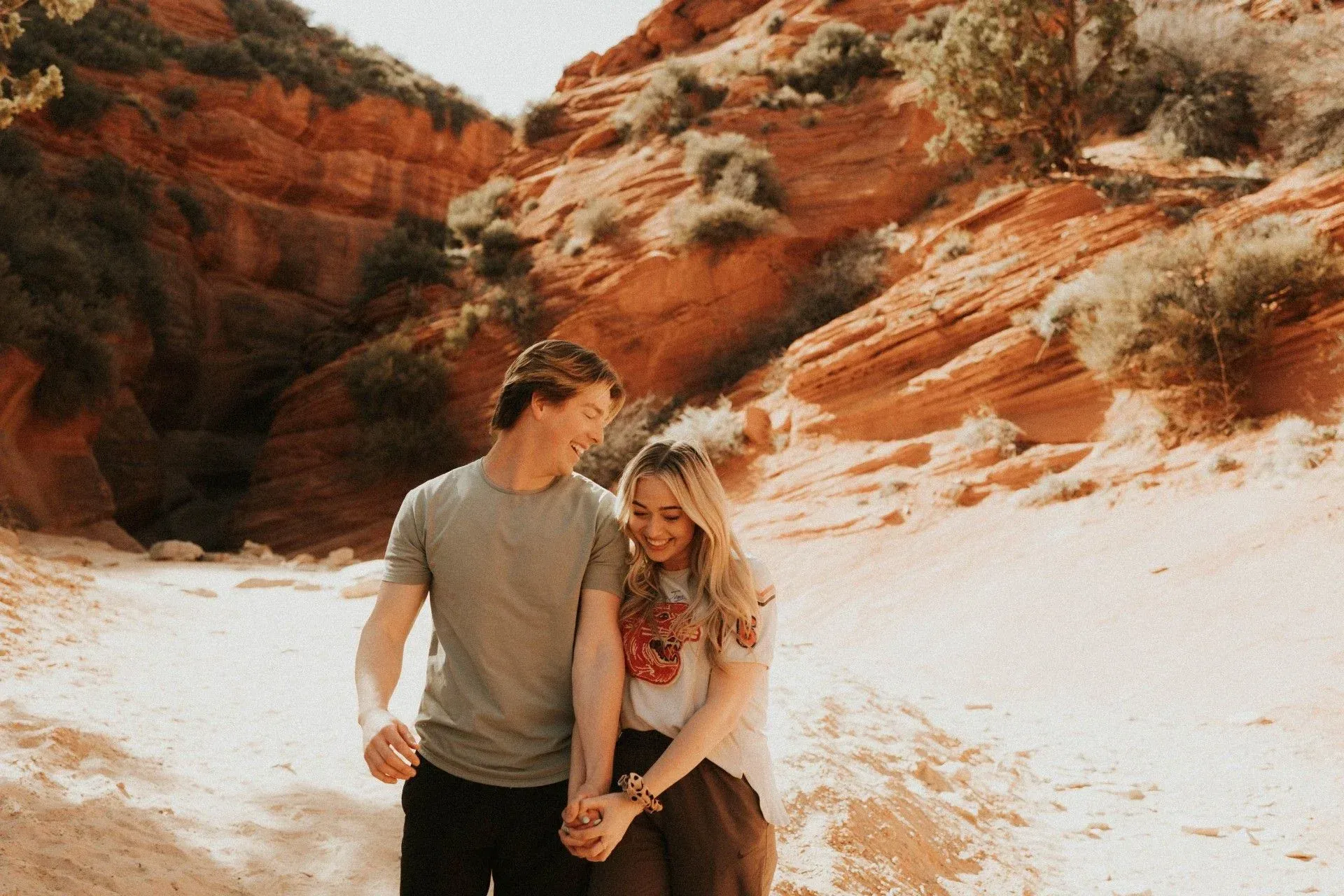 Couple walking hand in hand through a sunlit red rock canyon