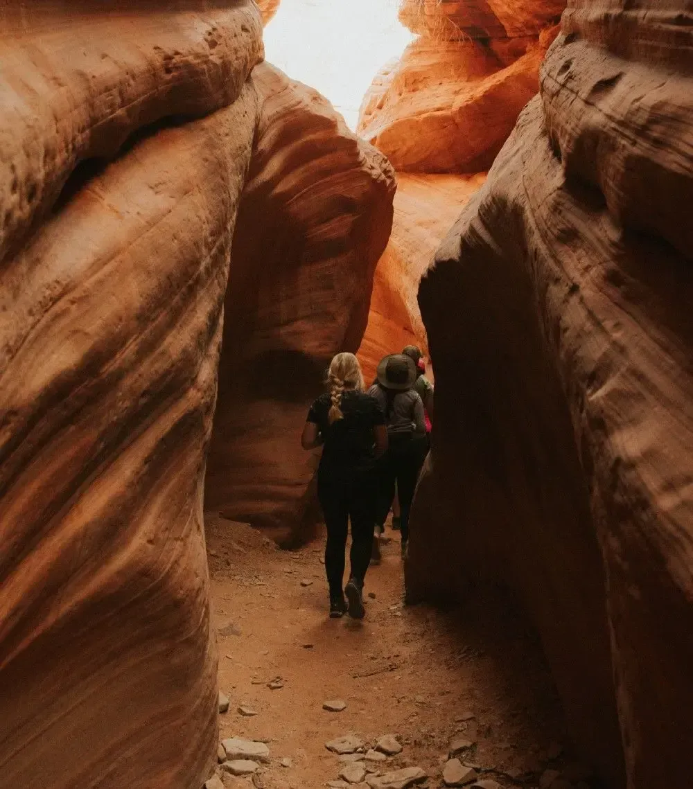 Two hikers walking through a narrow orange canyon corridor