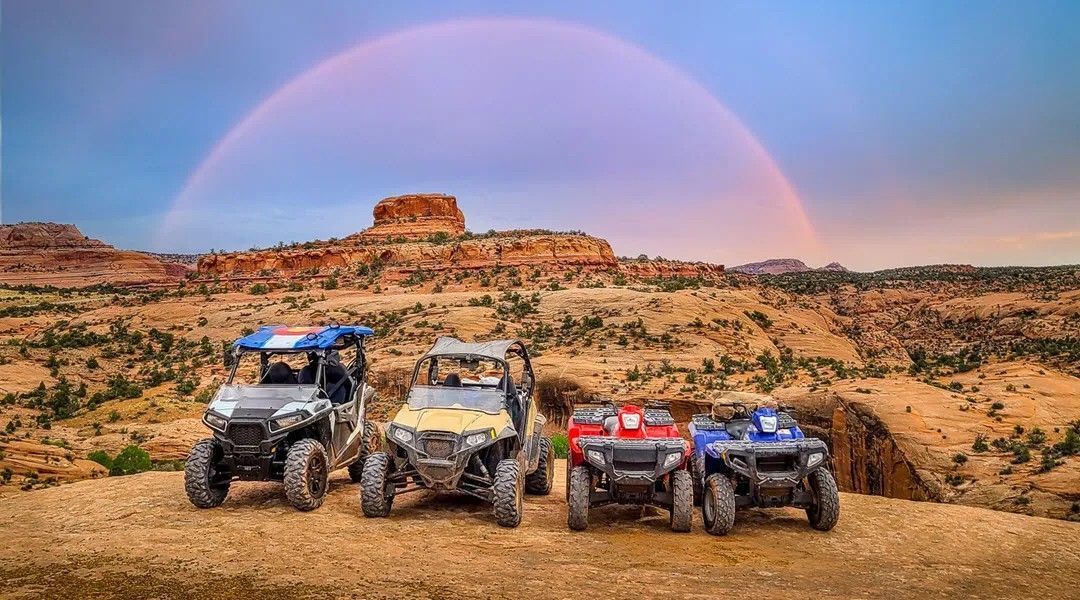 Three atvs are parked in front of a rainbow in the desert.