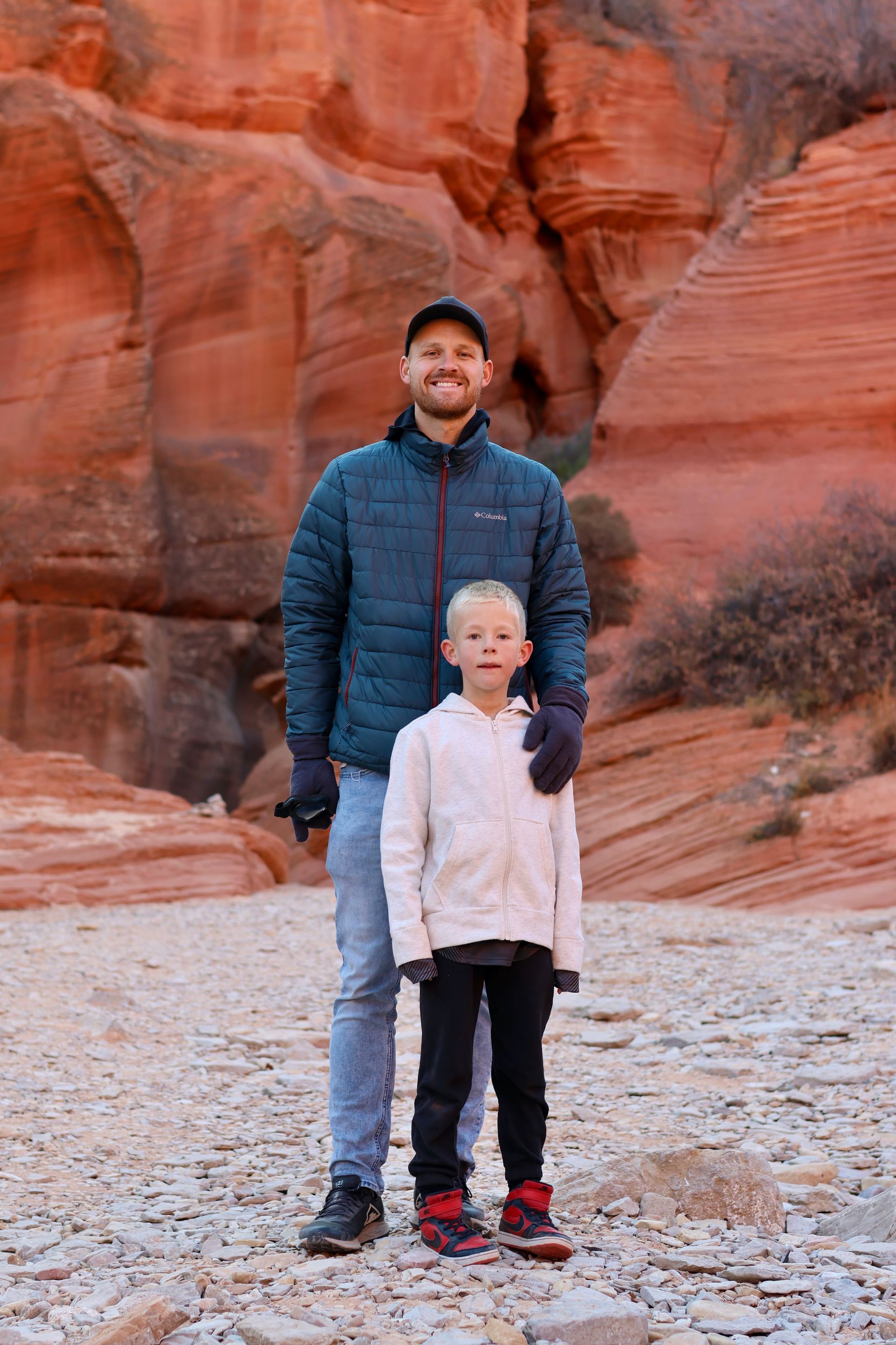A person smiles with their child in front of red rocks