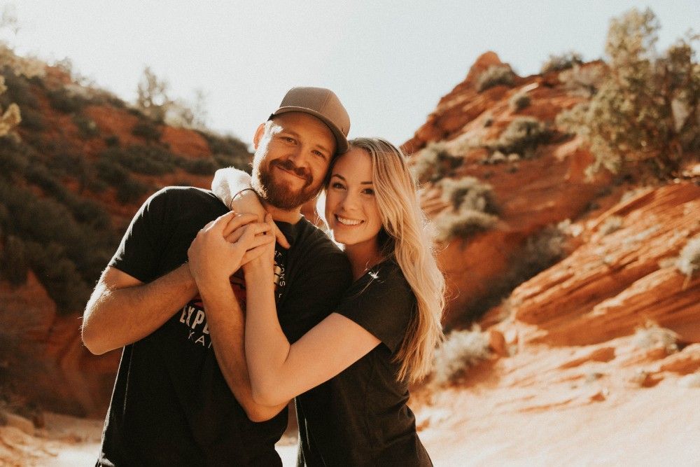 A man and a woman are hugging each other in front of a mountain.