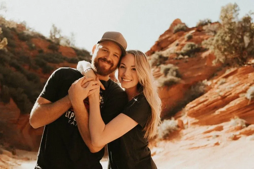 A man and a woman are hugging each other in front of a mountain.