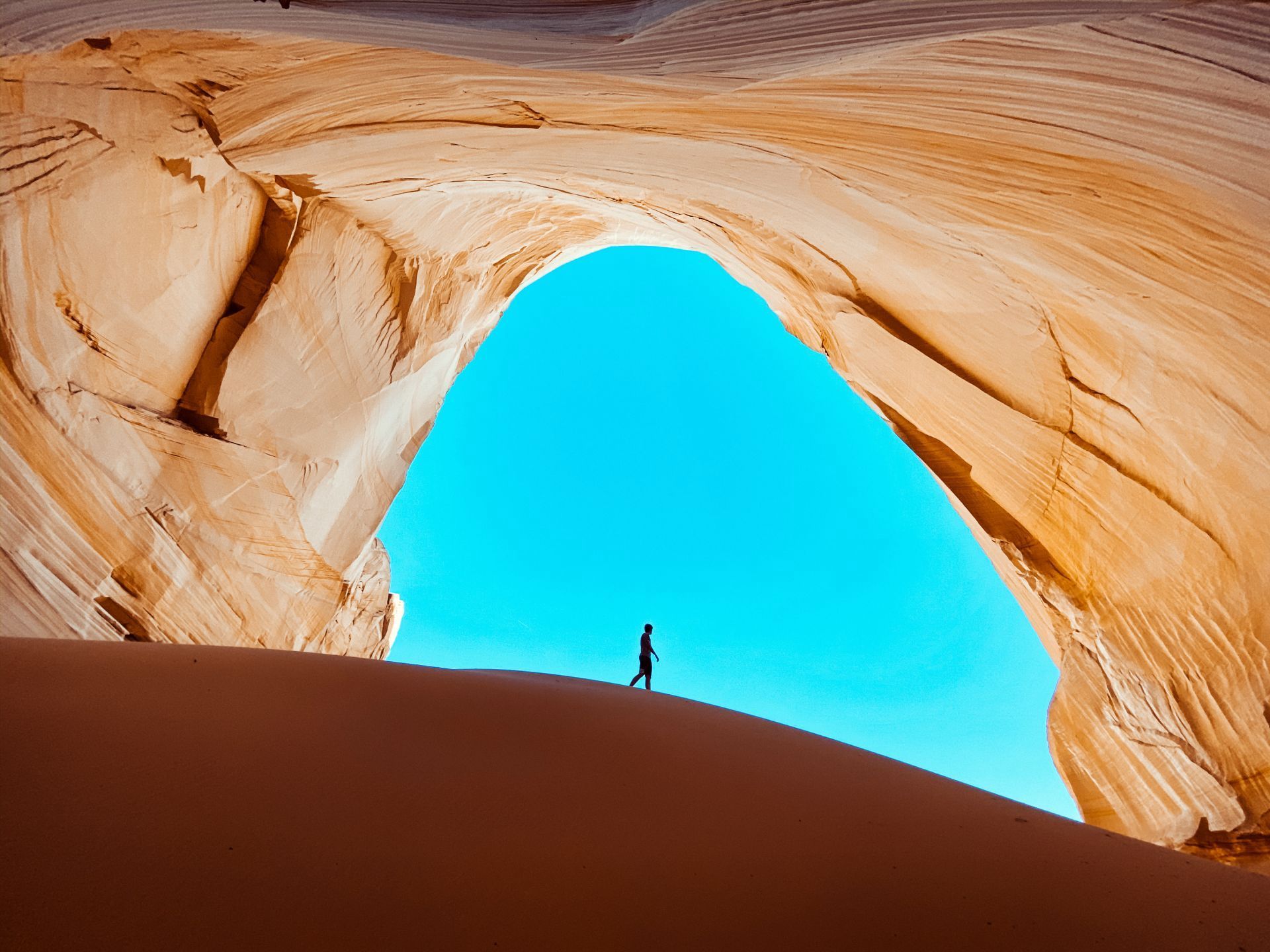 A man is standing on top of a sand dune in front of a cave.