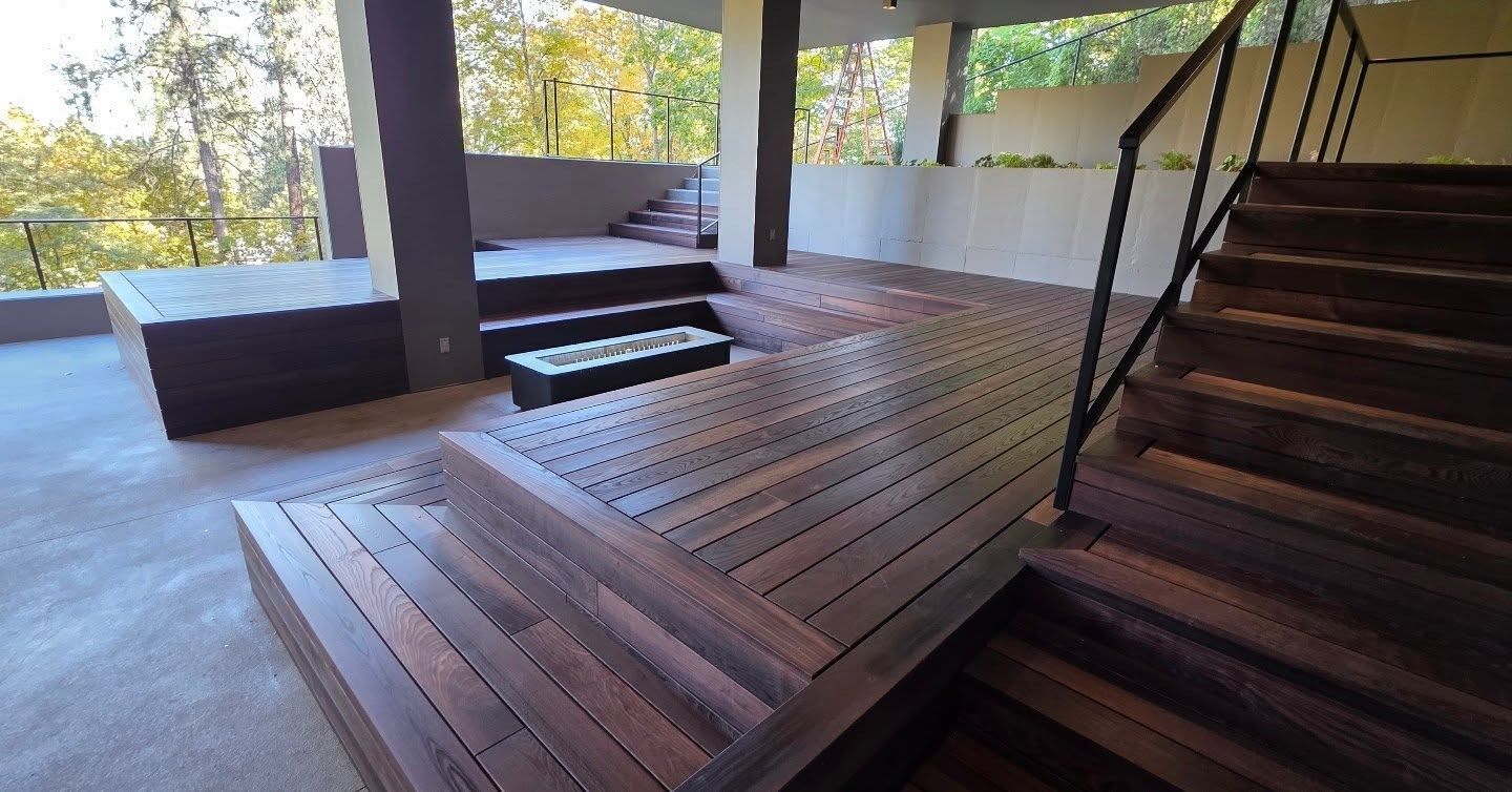 Wooden deck with stairs, built-in seating, and a modern fire pit, under a covered patio area.