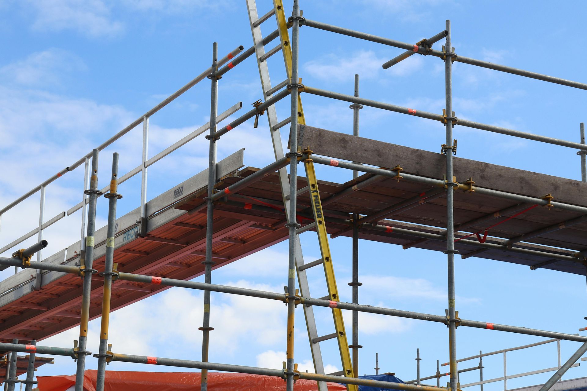 Scaffolding on construction site, gray metal frame with wooden planks, blue sky in background.