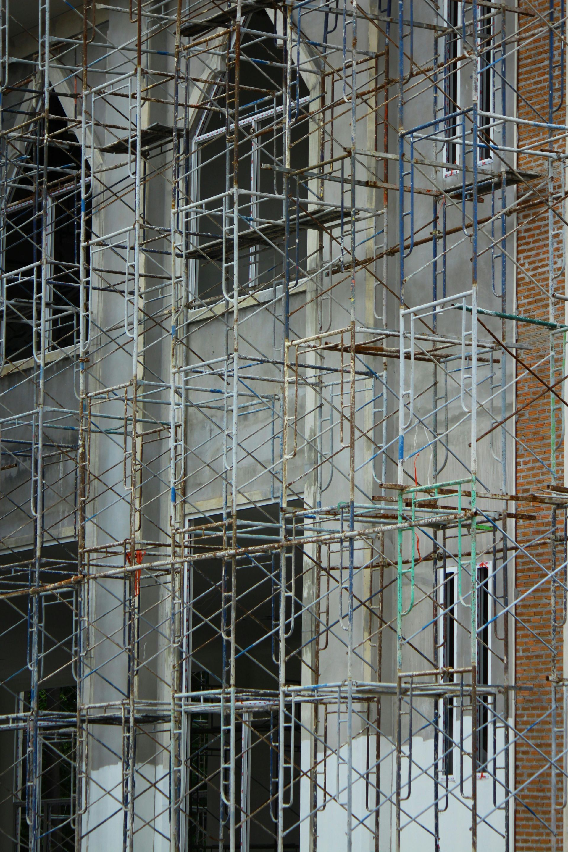 Building under construction with scaffolding. Gray concrete, brown brick, windows.