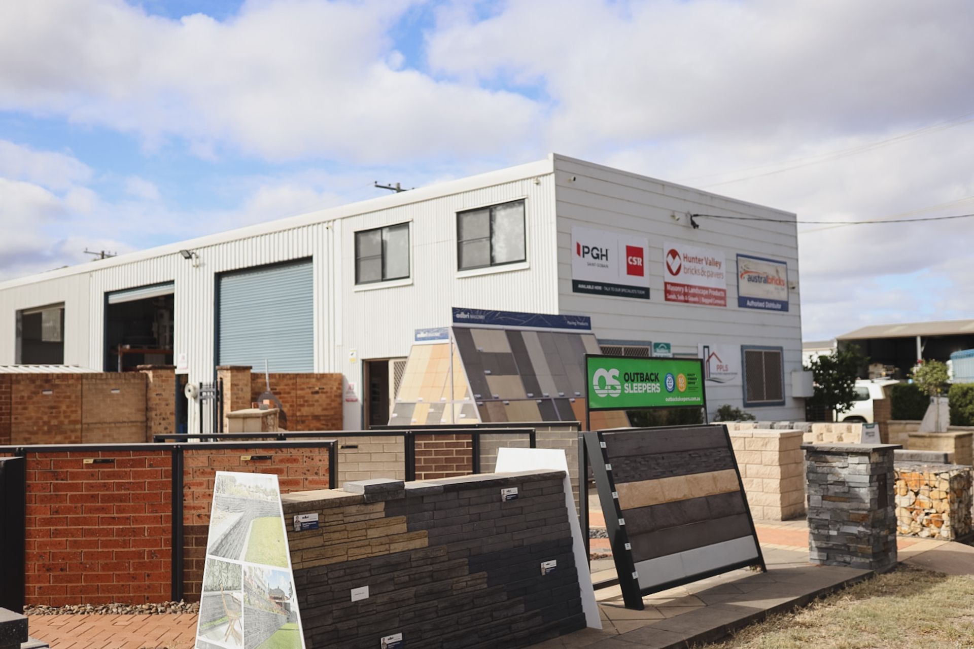 Industrial building with signage and stacked materials in a fenced lot under a cloudy sky— Hunter Valley Bricks & Pavers in Scone, NSW
