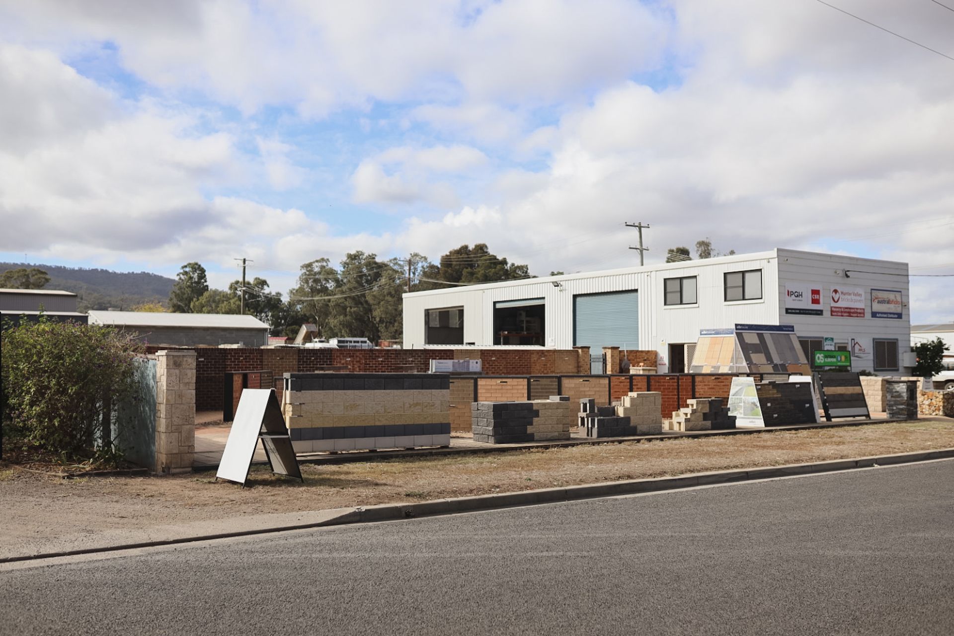 Outdoor yard with stacked wood, metal panels, and a white portable building under a cloudy sky— Hunter Valley Bricks & Pavers in Scone, NSW