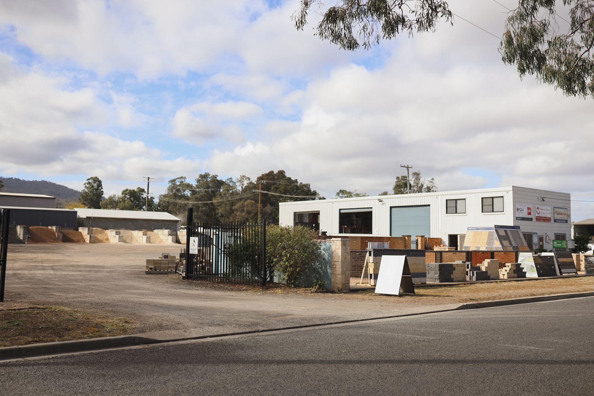 Street view of a construction site with a white building, fence, and signboards under a cloudy sky