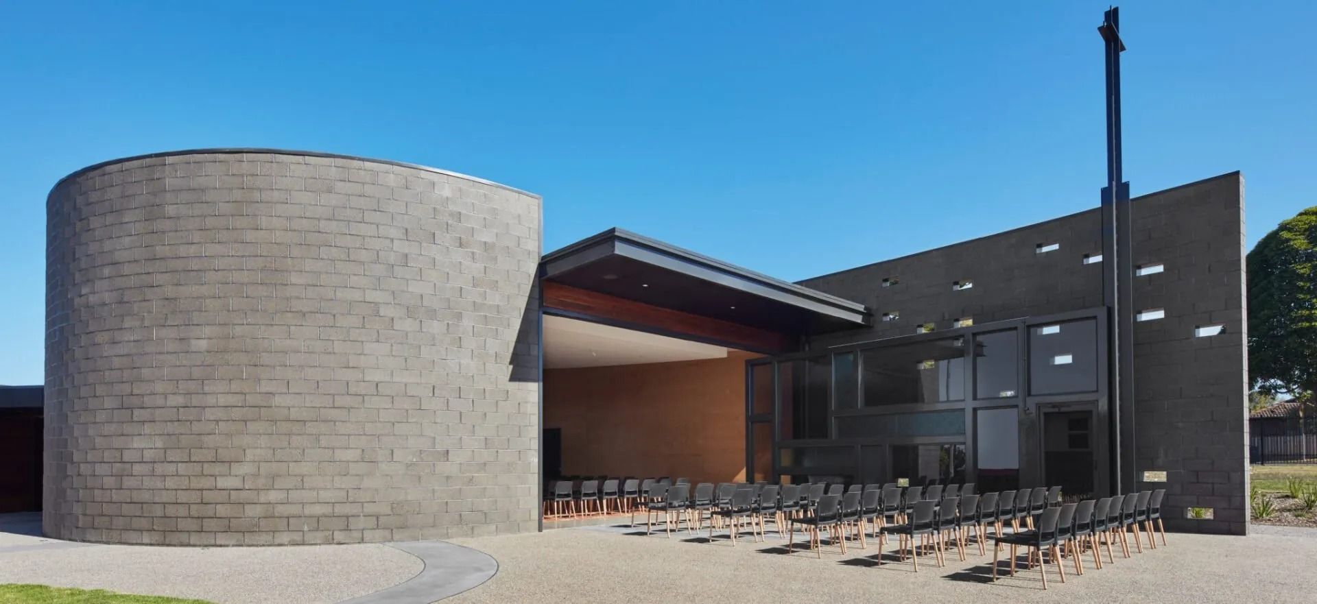 Modern Church Building With a Cylindrical Tower and Black Cross — Hunter Valley Bricks & Pavers in Scone, NSW
