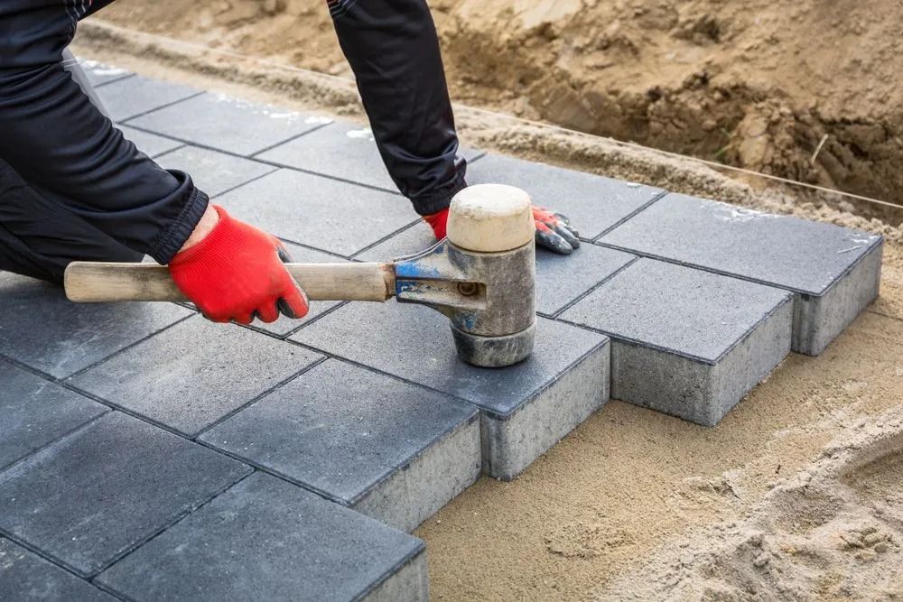Person Using a Rubber Mallet to Lay Grey Paving Stones — Hunter Valley Bricks & Pavers in Scone, NSW