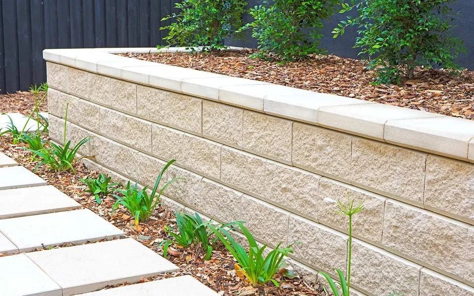 Beige Block Retaining Wall With Plants and Paving Stones — Hunter Valley Bricks & Pavers in Scone, NSW