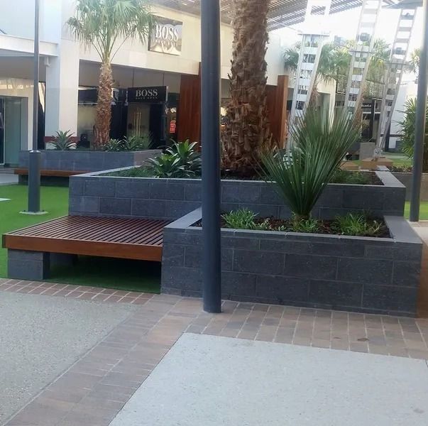 Outdoor Seating Area With Gray Brick Planters, Wooden Benches, and Palm Trees — Hunter Valley Bricks & Pavers in Scone, NSW