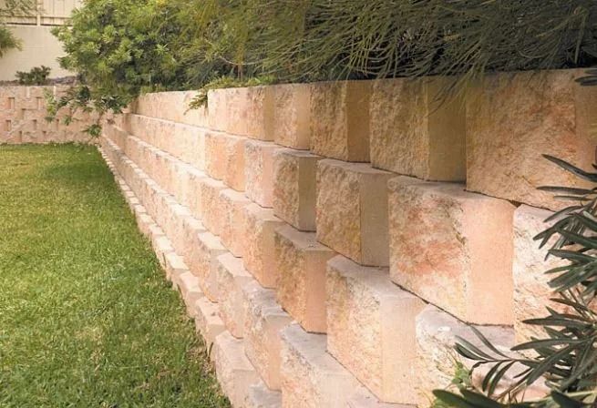 Stone Block Retaining Wall in a Backyard With Green Grass and Foliage — Hunter Valley Bricks & Pavers in Scone, NSW