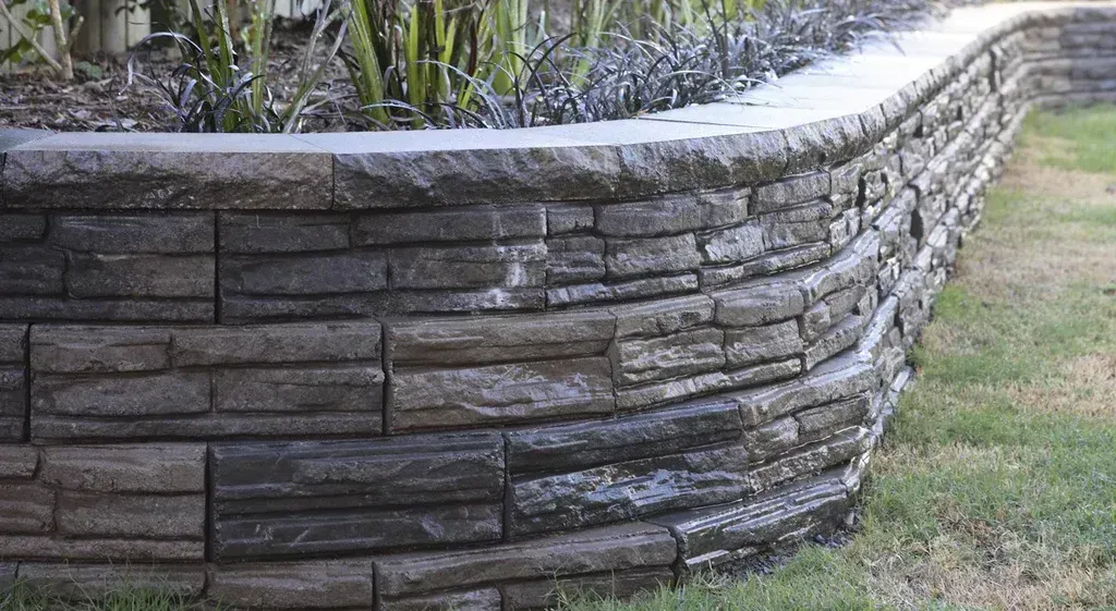 Curved Retaining Wall Made of Dark Stone Blocks, Edging a Grassy Area — Hunter Valley Bricks & Pavers in Scone, NSW