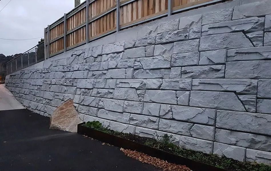 Gray Stone Retaining Wall With Wooden Fence Above; Small Plants Below — Hunter Valley Bricks & Pavers in Scone, NSW