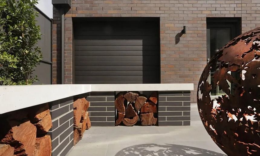 Exterior With Brick Building, Garage Door, and a Firewood Storage Area — Hunter Valley Bricks & Pavers in Scone, NSW