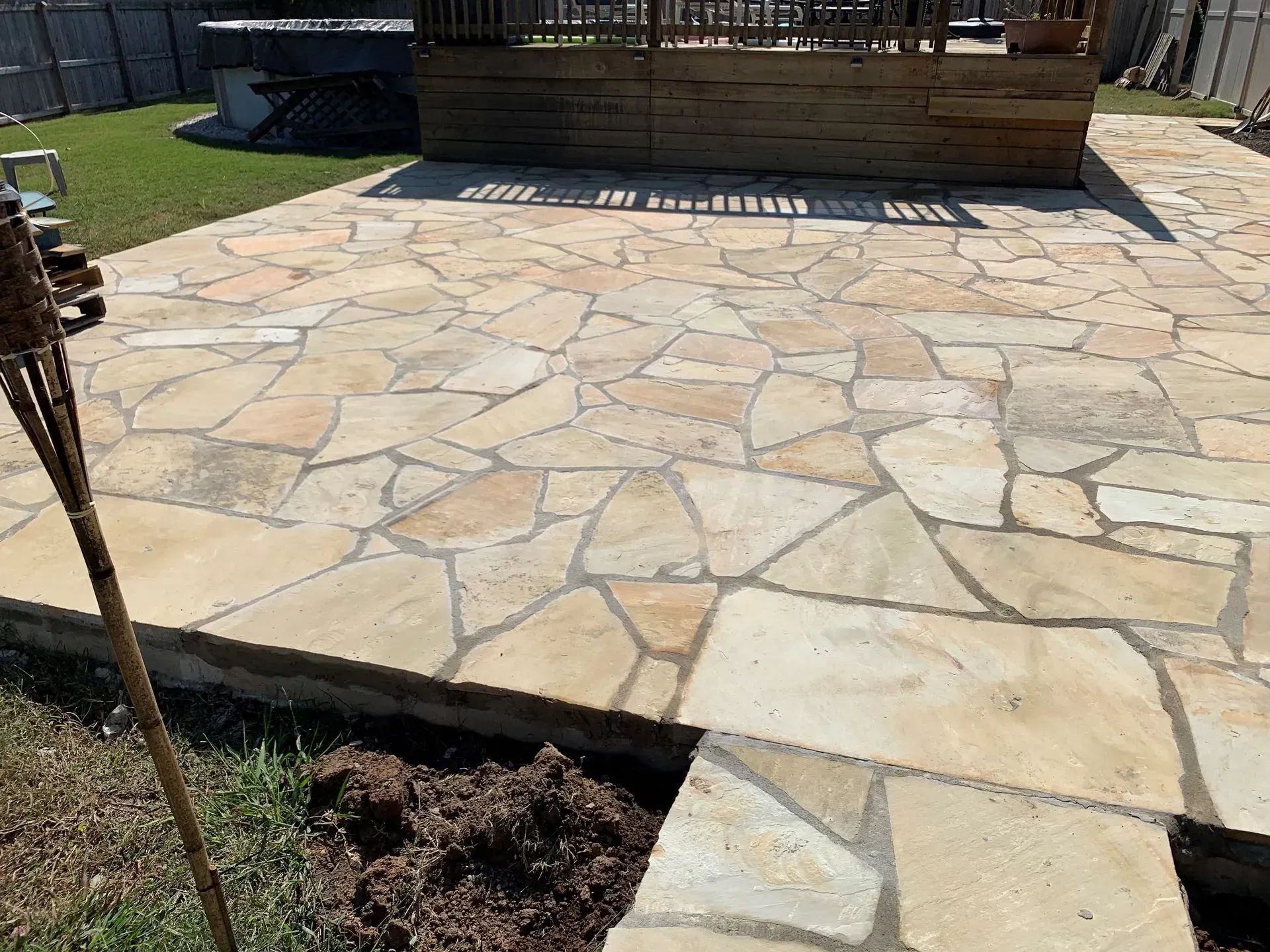 Stone patio with tan flagstones and a wooden deck in a yard.