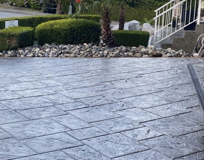 A concrete driveway with stairs and bushes in the background.