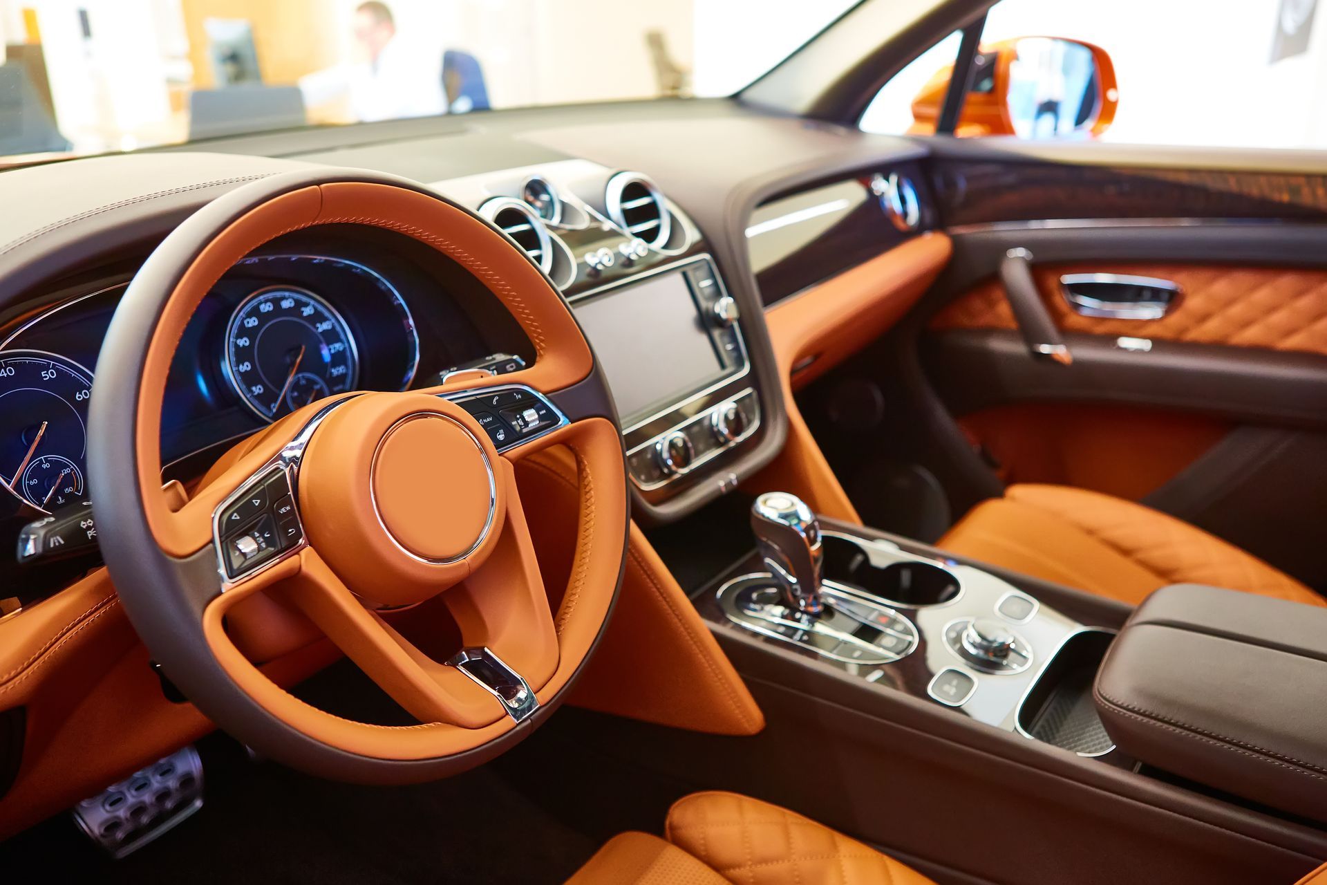 Orange leather interior of a luxury car, including steering wheel, dashboard, and seats.