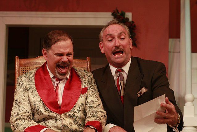 Man wearing dressing gown with red trim sitting next to man in dark suit and tie