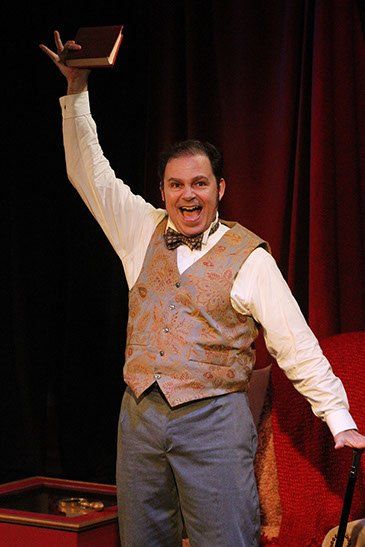 Man with dark hair wearing colorful vest and holding booking one hand and cane in the other