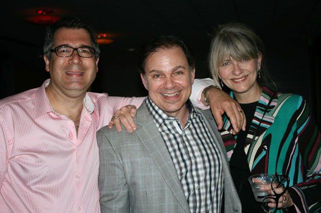 Man in pink shirt, man in grey jacket and woman in colorful scarf posing for picture