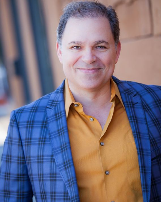 Phil, smiling, wearing blue checked suit jacket and gold shirt