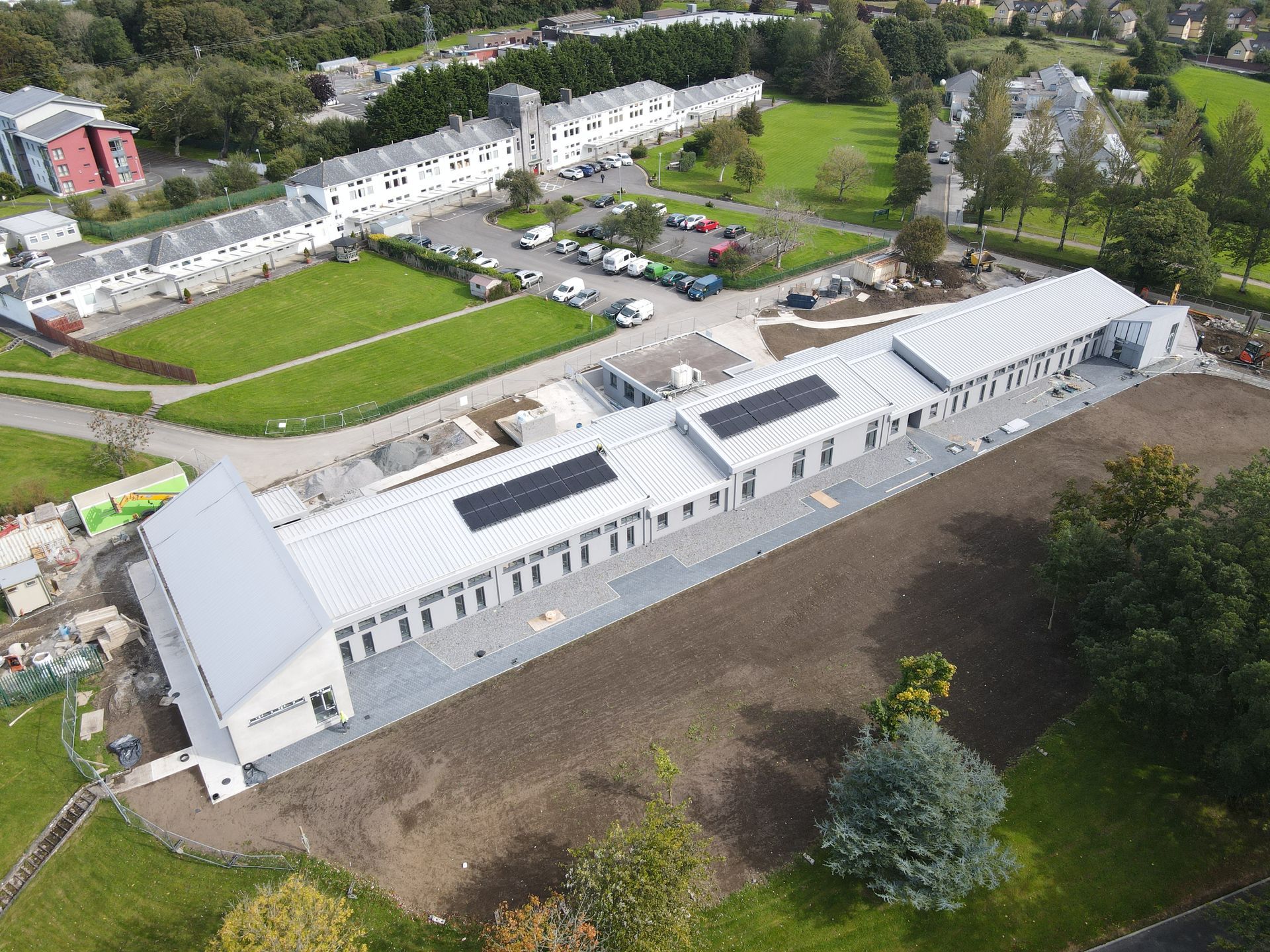 An aerial view of a large building with solar panels on the roof surrounded by trees.