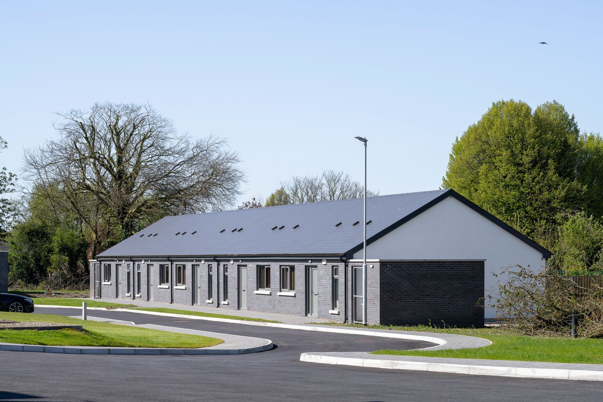 A white building with a black roof is surrounded by trees