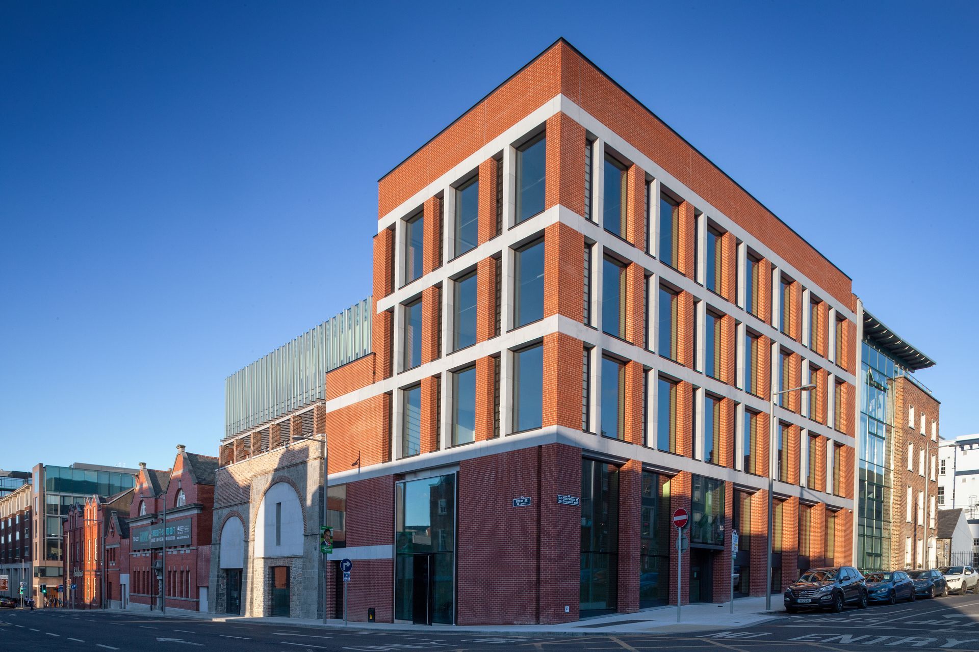 A large brick building with a lot of windows is on the corner of a city street.