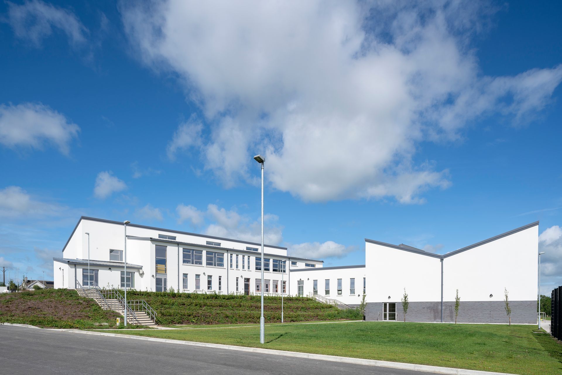 A large white building is sitting on top of a grassy hill.