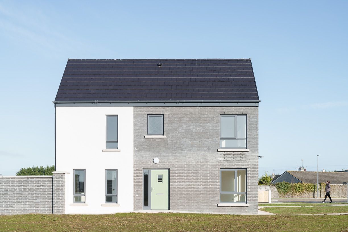 A white and gray house with a black roof is sitting on top of a lush green field.