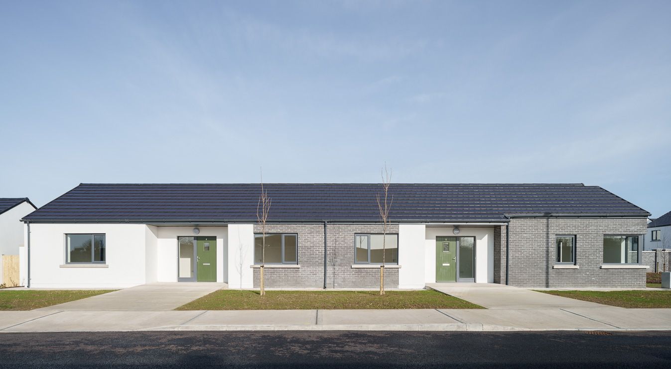A white house with a black roof and green doors is sitting on the side of the road.
