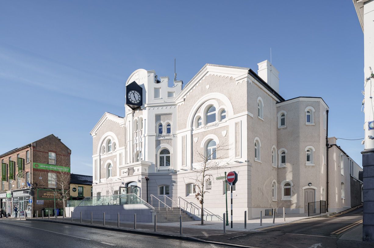 A large white building with a clock on top of it is on the corner of a street.